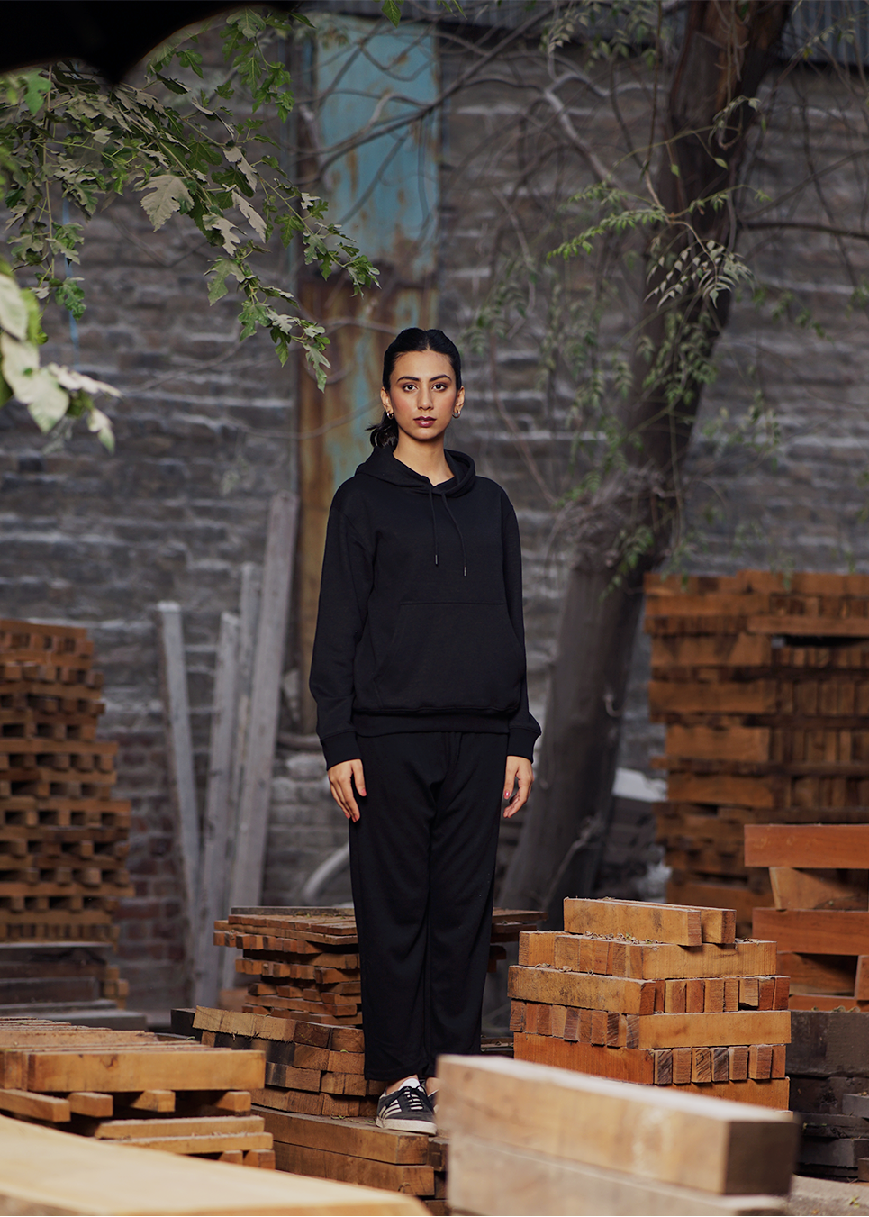Woman wearing a black hoodie standing among wooden pallets.